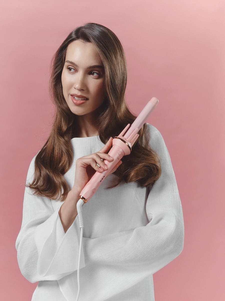 Woman holding a pink hair straightener against a pink background