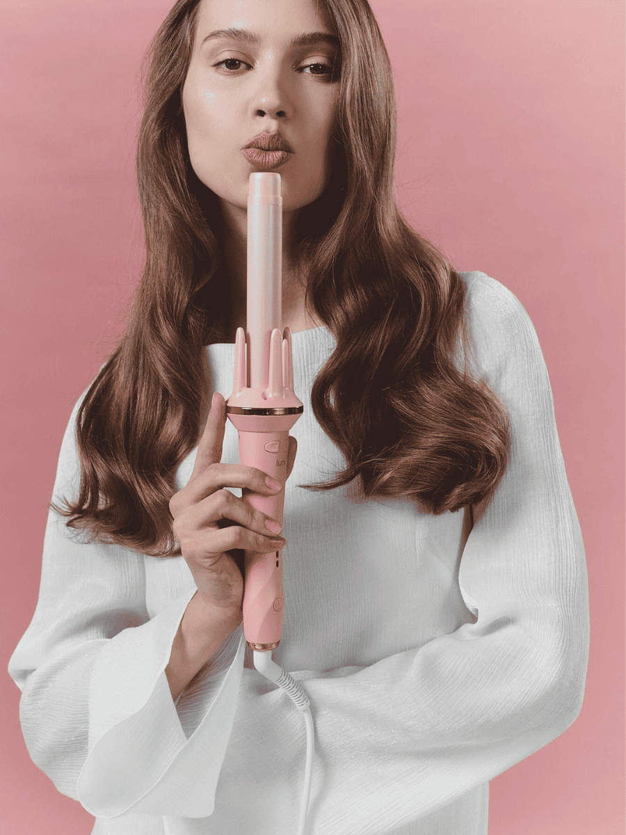 Woman holding a pink hair curler against a pink background