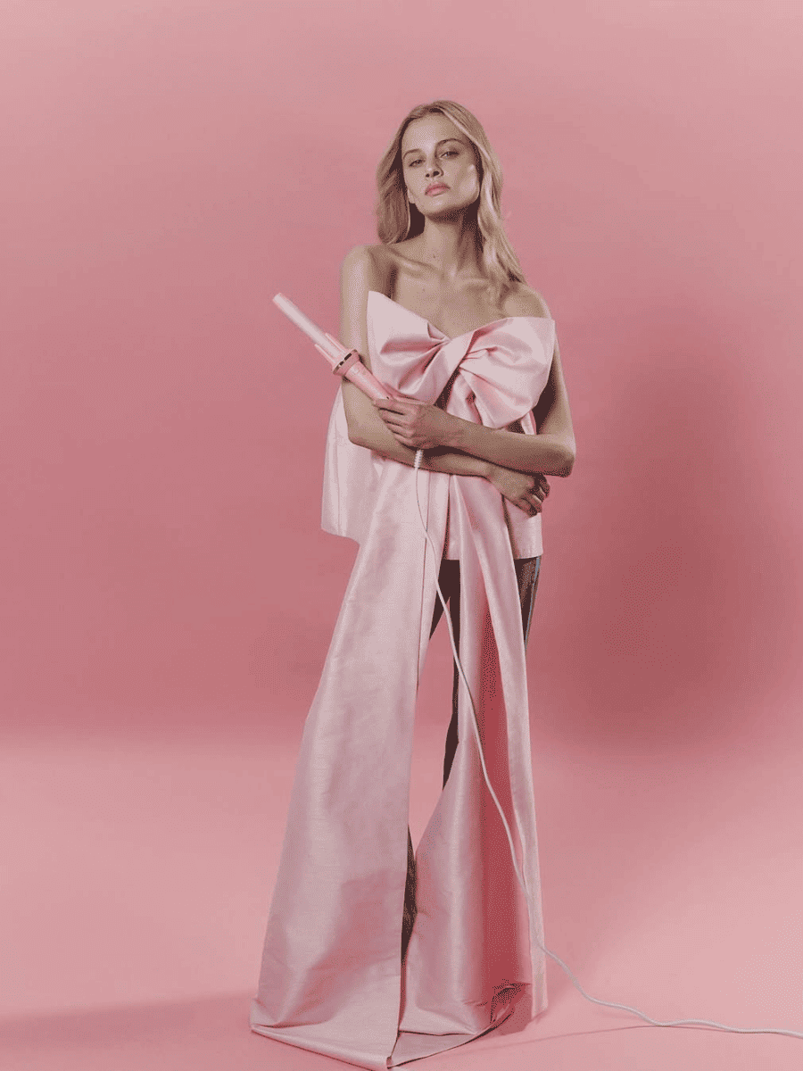 Woman wearing a pink strapless dress with a large bow on a pink background