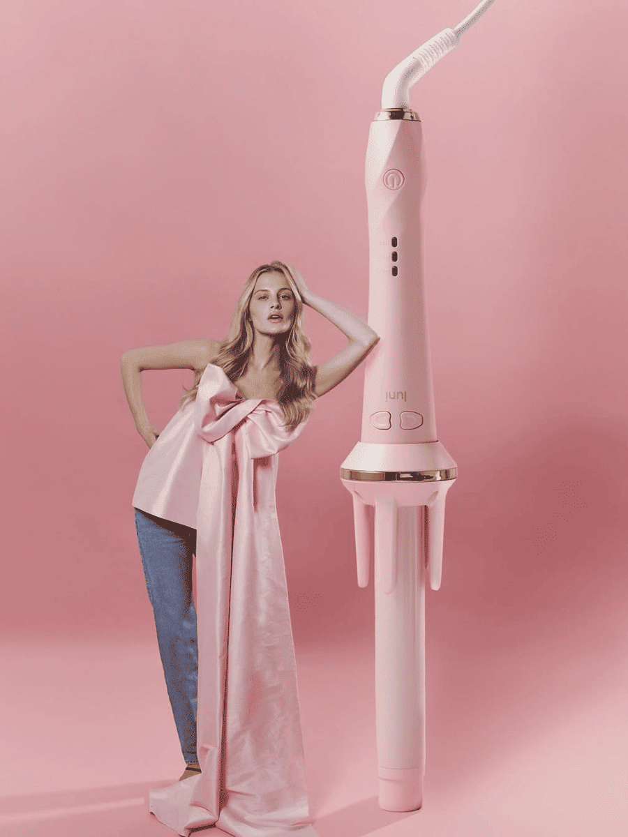 Woman holding a long pink bow next to a pink hair straightener on a pink background