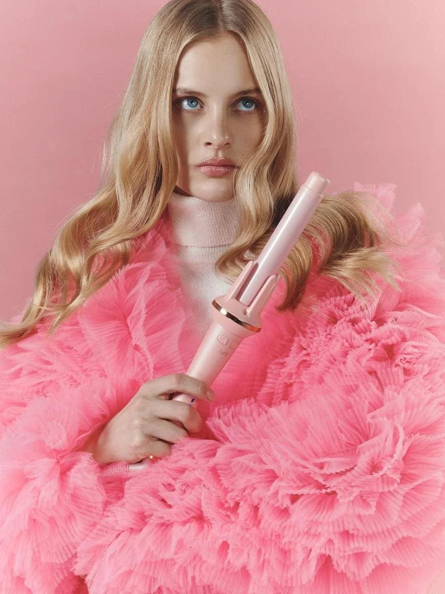 Woman holding a pink hair curler against a pink background