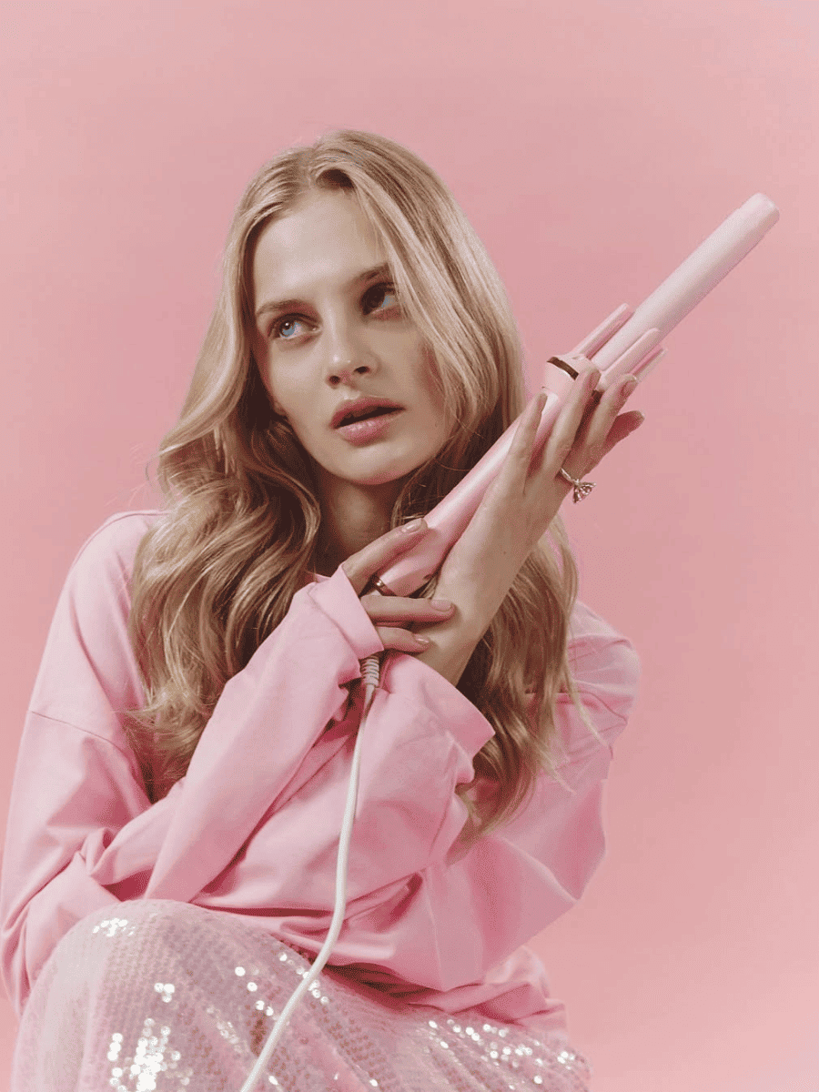 Woman holding a white hair straightener against a pink background