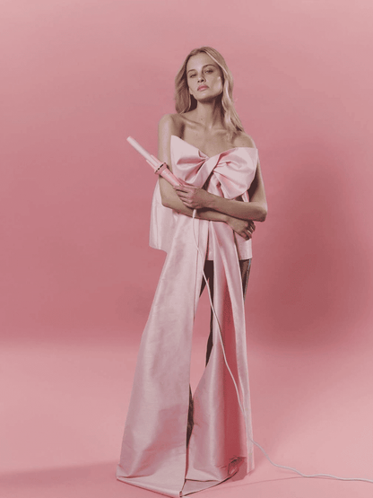Woman wearing a pink strapless dress with a large bow on a pink background