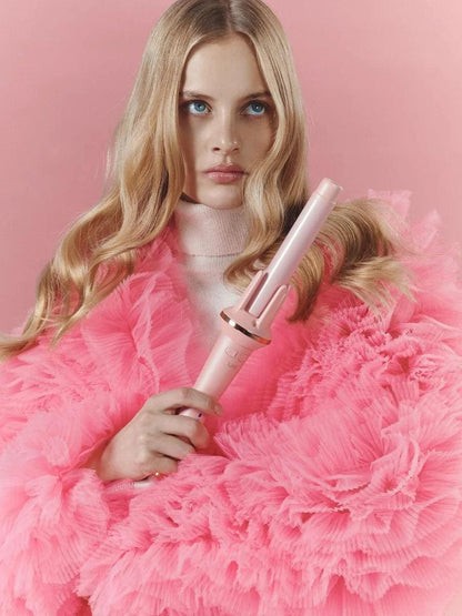 Woman holding a pink hair curler against a pink background